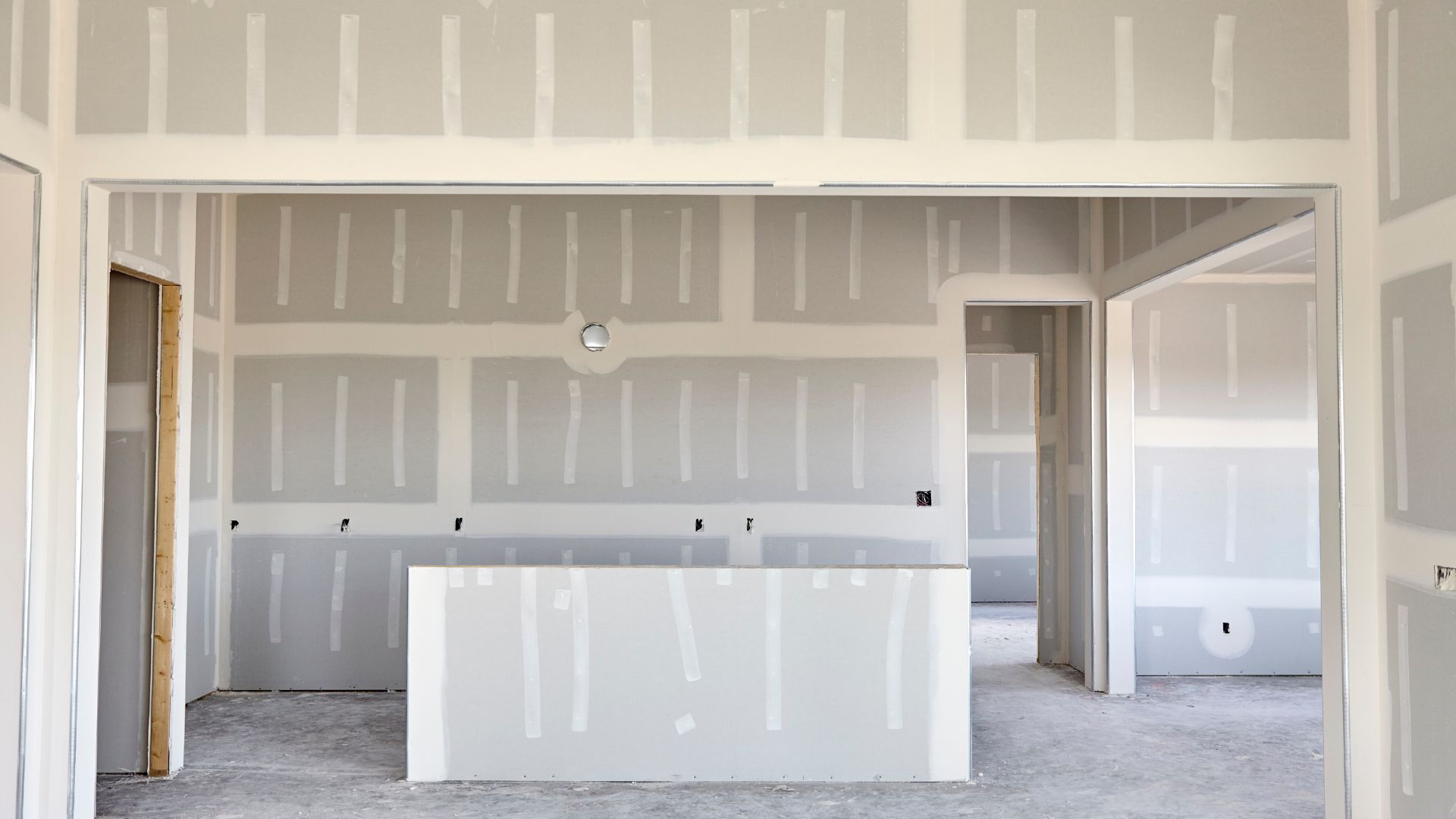 Unfinished interior room with drywall, white walls, and concrete floor