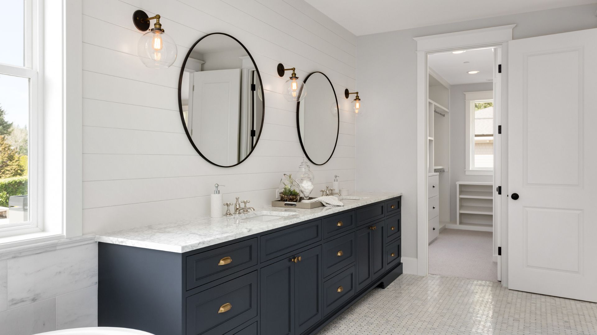 Modern bathroom with navy vanity, oval mirrors, and vintage wall sconces