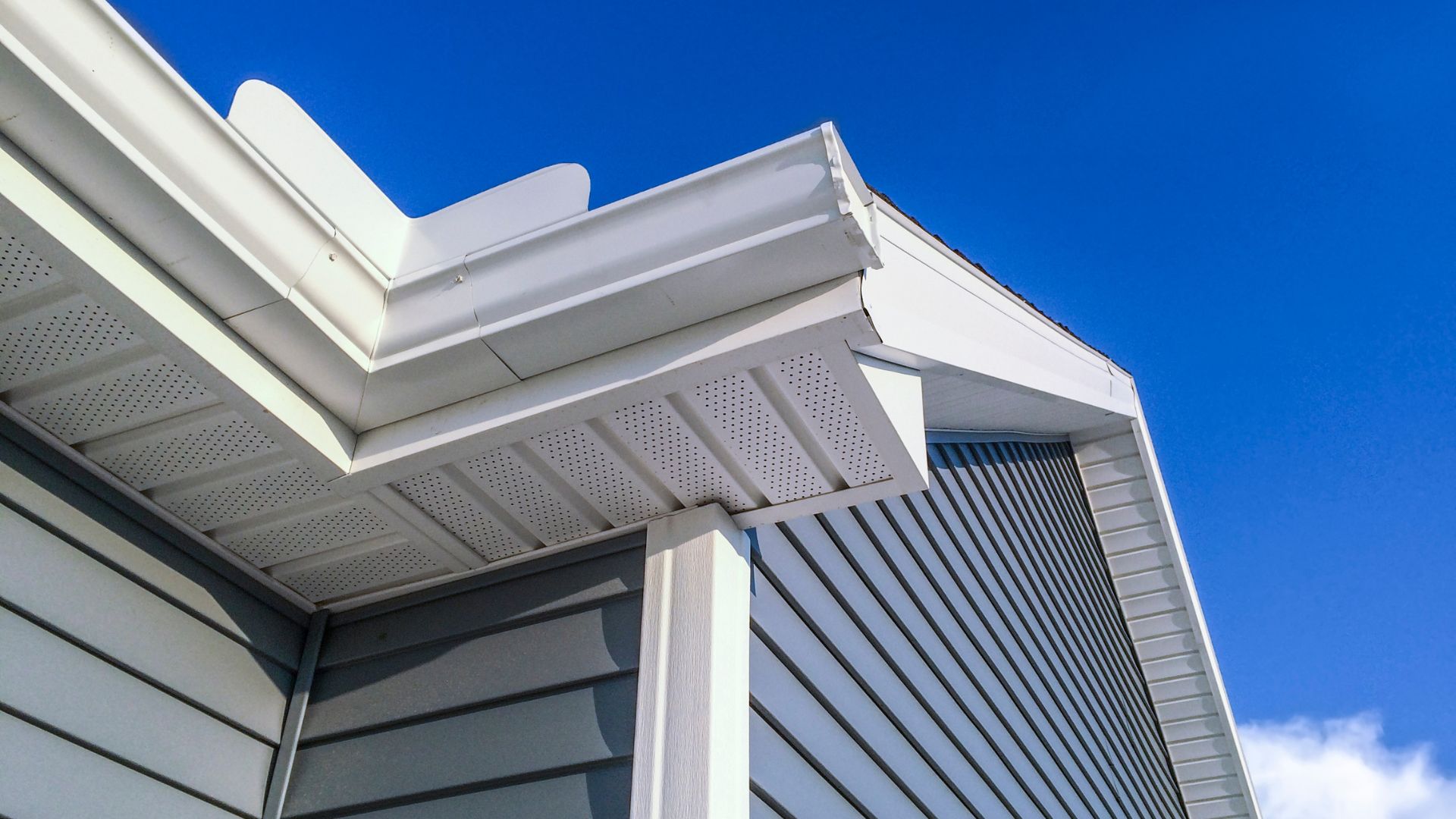 White architectural roof detail with perforated soffit against bright blue sky