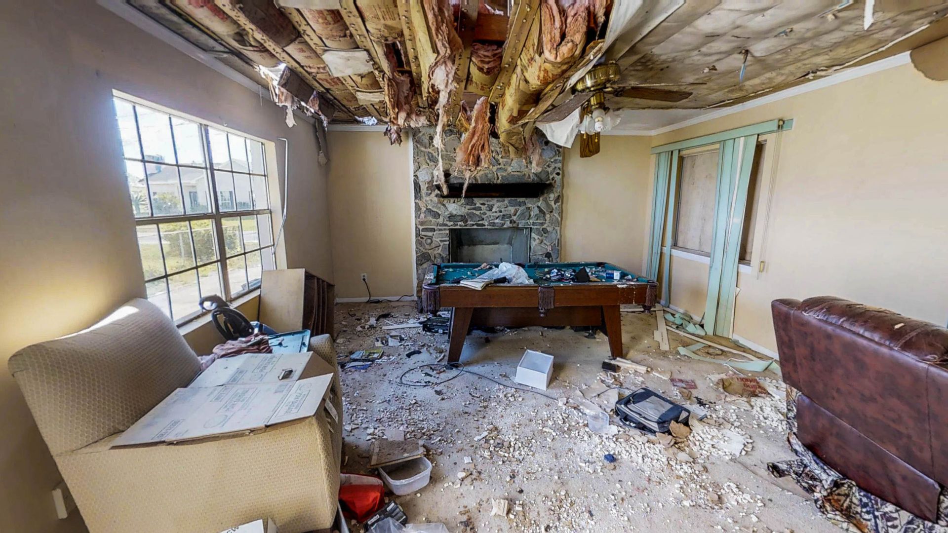 Severely damaged interior room with debris, pool table, and falling ceiling