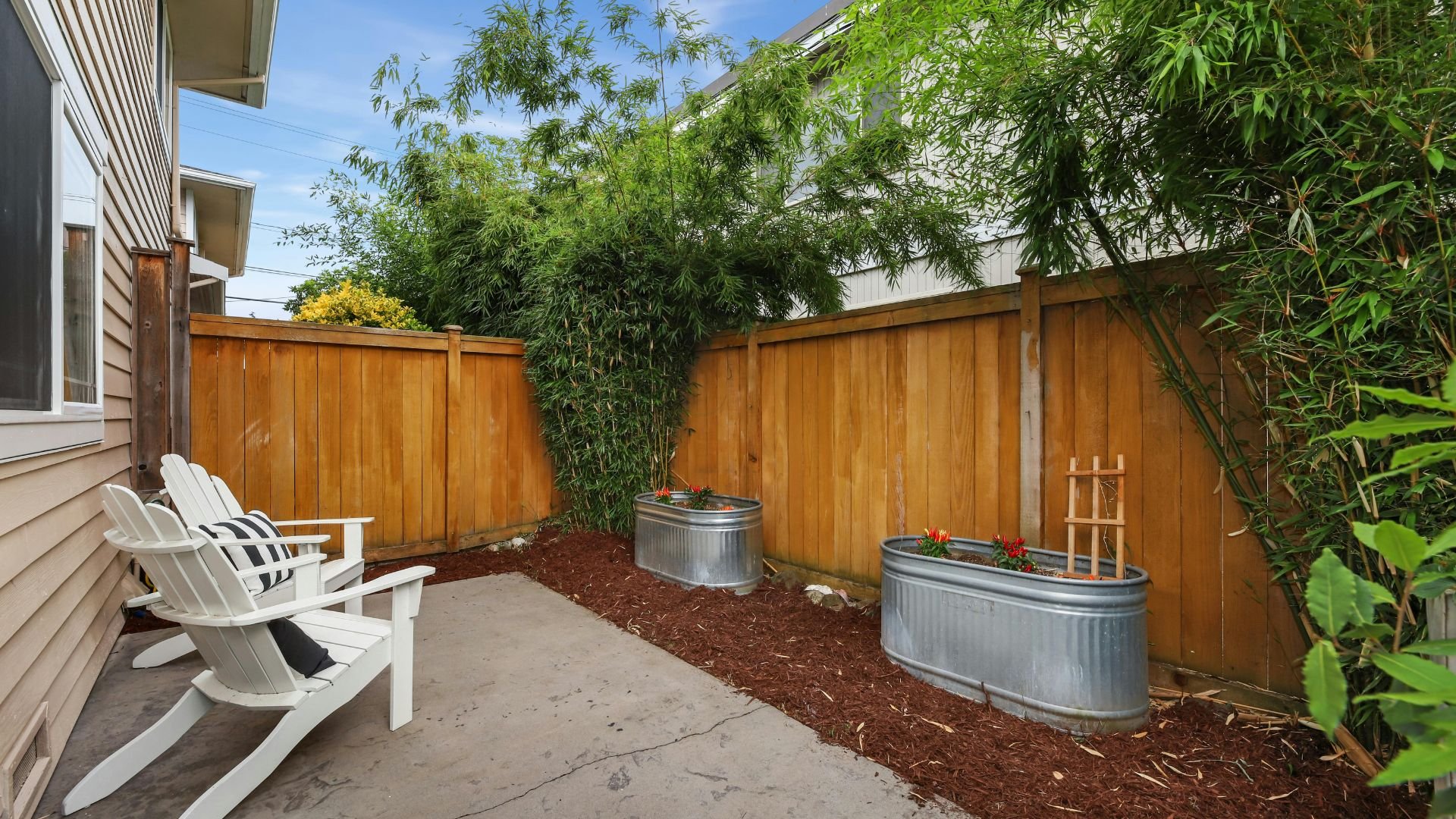 Cozy backyard with white Adirondack chairs, metal planters, and wooden fence